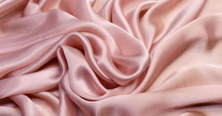 Soft pink fabric draped smoothly, illustrating what is charmeuse silk.