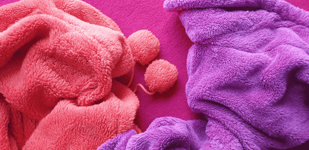 Folded pink and purple fleece blankets with pom-poms