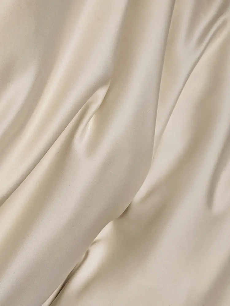 Close-up of creamy white satin modal fabric with gentle folds, illustrating a soft, silky surface.