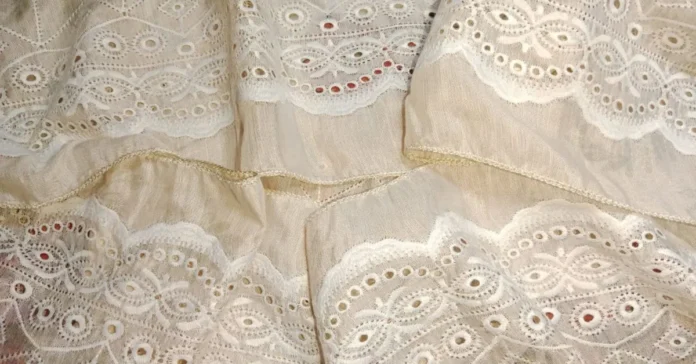Close-up of beige Cotton Eyelet fabric with oval and circular embroidery patterns