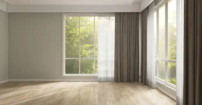 Gray drapes and white sheer curtains framing large corner windows in an empty living room with wooden flooring